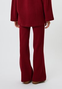 Bordeaux geribbelde loungewearset bestaande uit een los vallend shirt en uitlopende broeken, gemaakt van zacht materiaal met een gladde textuur en lange mouwen.