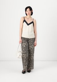 Camiseta de tirantes en crema y negro con escote en V, combinada con pantalones de pierna ancha de estampado de cebra, sosteniendo un bolso blanco y usando zapatos negros.
