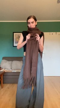 Écharpe brune avec des bords à franges, en tissu doux, drapée confortablement autour du cou, accompagnée d'un pantalon large gris.