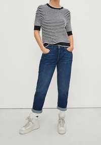 Gestreepte korte mouwen trui in marineblauw en wit, gecombineerd met een relaxed-fit donkerblauwe jeans, opgerold bij de enkels, en witte high-top sneakers.