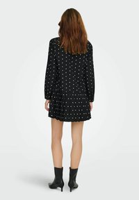 Juoda suknelė su ilgomis rankovėmis, baltais rutuliukais, klostuota sijono dalimi ir užsegimu gale su sagomis. Dėvima su juodais aulinukais. Lygus audinio tekstūra.