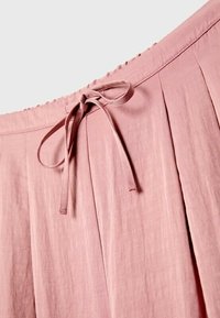 Pantalon en tissu rose avec une taille à cordon noué et des plis doux, mettant en valeur la ceinture et le détail du haut.