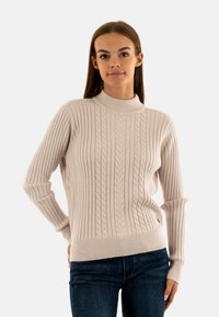 Maglione a costine crema con collo alto, caratterizzato da un motivo a trecce e maniche lunghe. Realizzato in un morbido tessuto testurizzato.