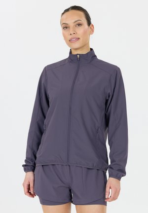 Veste légère violette avec col montant, fermeture éclair sur le devant et poignets élastiques. Elle comprend deux poches latérales et une texture lisse et mate.