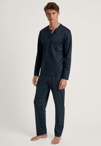 Navy blauw langemouwshirt met een zak en knoopdetail, gecombineerd met gestreepte pyjamabroek met blauwe en paarse motieven op een donkere achtergrond.