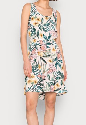 Ärmelloses Blumenkleid mit gelben und pinken Blumen sowie grünen Blättern, in der Taille gerafft, getragen von einer Frau, die vor einem hellen Hintergrund steht.