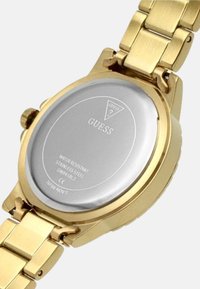 Kultainen ruostumattomasta teräksestä valmistettu kello, jossa on linkitetty ranneke. Varustettu pyöreällä hopeanvärisellä takana, johon on kaiverrettu brändi ja tekniset tiedot.