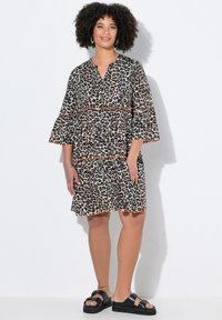 Vestido estampado de leopardo con un corte relajado, escote en V y mangas acampanadas, con ribete naranja en la cintura y el dobladillo. Combinado con sandalias negras.