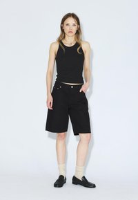 Top negro de tirantes combinado con pantalones cortos negros hasta la rodilla. El modelo lleva calcetines blancos y mocasines negros. Diseño simple, sin patrones ni acentos visibles.