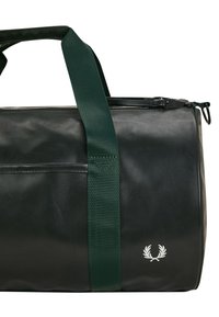 Borsa duffel verde realizzata in materiale resistente e testurizzato. Presenta robuste cinghie verde scuro e un logo bianco sul lato. Chiusura superiore con zip.