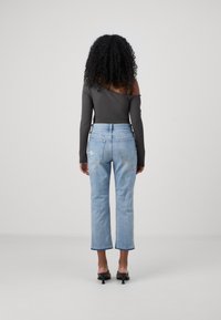 Šedý top bez ramínek s dlouhými rukávy, spárovaný s světle modrými džíny s rovnými nohavicemi, s vybledlým vzhledem a jemnými detaily na zadních kapsách.