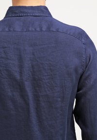 Marins blå linne skjorta med avslappnad passform, som har en knapp-down krage och subtil textur, synlig sömnad längs sömmarna.