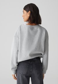 Grauer, übergroßer Sweatshirt mit Rundhalsausschnitt und fallenden Schultern. Kombiniert mit dunkelgrauen Jeans mit Gesäßtaschen. Weiche Stofftextur.