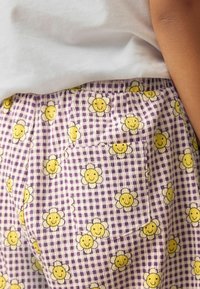 Lila Gingham-Shorts mit einem sich wiederholenden Muster von gelben lächelnden Blumen. Enthält eine Seitentasche und besteht aus leichtem Stoff.