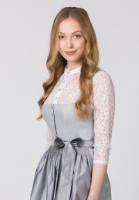 Das Kleid hat ein graues Oberteil mit Knopfdetails und einen satinartigen Rock, kombiniert mit einer weißen Bluse mit langen Ärmeln aus Spitze. Eine Schleife an der Taille.