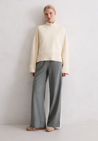 Kremowy, wysoki sweatshirt z luźnymi, szarymi spodniami szerokimi w nogawkach. Miękka tkanina, swobodny krój i minimalne detale na obu elementach.