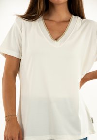V-hals T-shirt van off-white stof, met korte mouwen en een contrasterende gouden rand rond de halslijn. Gladde textuur, ontspannen pasvorm.