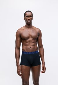 Fekete boxer alsónadrág kék derékkal, melyen a "HILFIGER" logó található. Az anyag sima megjelenésű, testhez álló kialakítással és funkcionális elülső nyitással rendelkezik.