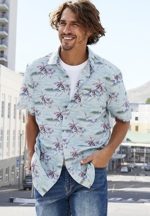 Short-sleeve button-up shirt featuring a light blue background with pink palm tree and ocean wave patterns. Worn over a white t-shirt.