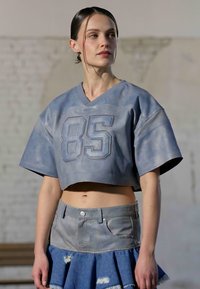 Camiseta azul cortada con textura de malla y el número "85" en el pecho, combinada con una falda mini de mezclilla con detalles desgastados.