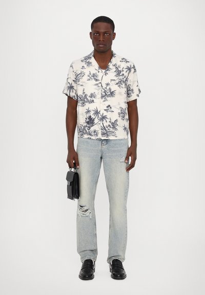 Kortærmet hvid skjorte med marineblåt tropisk print, parret med slidte lyseblå jeans. Tilbehør inkluderer en lille sort taske og sorte sko.