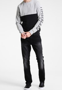 Grijs-zwart colorblock sweatshirt met Timberland-logo op de mouw, gecombineerd met vervaagde zwarte jeans en zwarte sneakers.