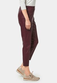 Bordeaux lederen broek met een slim fit en taps toelopende enkels. Gepaard met beige sneakers met patronen en veters.