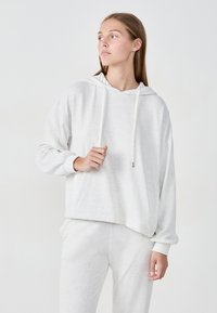 Sudadera gris claro con mangas largas y capucha con cordón. Textura suave, corte relajado y puños acanalados. Combinada con pantalones a juego en gris claro.