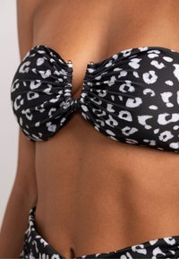 Top bikini bandeau nero con stampa leopardata bianca. Presenta un tessuto arricciato e una chiusura centrale in metallo dorato per un fissaggio sicuro.