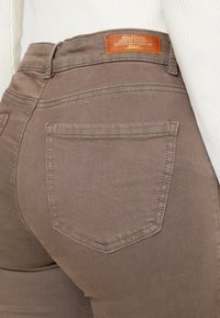 Brązowe dżinsy o slim fit, z tylnią kieszenią z subtelnym wzorem szwów oraz skórzaną metką marki na pasku.