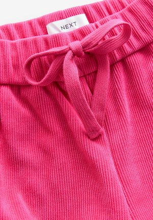 Shorts de tela acanalada rosa con cintura ajustable. La textura es suave, con una etiqueta de marca visible que dice "NEXT" cerca de la parte superior.