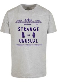 Pelēka kokvilnas T-krekls ar purpura krāsā izsistiem vārdiem: "Es pats esmu DĪVAINA un NEPARASTA" un divām spokiem, kā arī vārdu "BEETLEJUICE", kas atkārtojas zemāk.