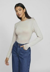 Ljusbeige långärmad topp i mjukt tyg, kombinerad med högmidjade mörkblå denimbyxor med fickor och kontrastsömmar.