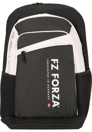 Mand i sort sportstøj står med en sort og hvid FZ FORZA rygsæk, kigger til siden og smiler foran en ensfarvet baggrund.
