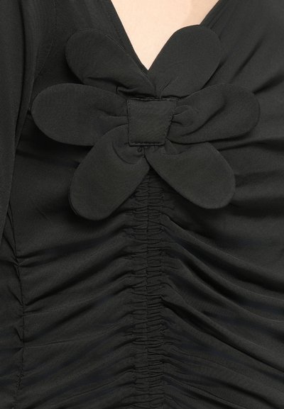 Fekete ruha, amelynek nyakán nagy, szövetből készült virágdísszel rendelkezik. Az elülső részen ráncolt, texturált anyag található az extra dizájn érdekében.