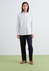 Striped button-up skjorte i hvit og grå, med brystlomme. Kombinert med mørke bukser og brune sko. Enkelt, avslappet design.
