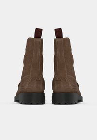 Bottines en daim marron avec une semelle en caoutchouc noir, dotées de languettes de tirage marron et de coutures renforcées le long des coutures pour plus de durabilité.