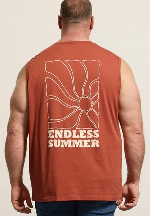Mann trägt ärmelloses, rostfarbenes Shirt mit weißem abstraktem Sonnenmotiv und Schriftzug „ENDLESS SUMMER“ auf dem Rücken, steht vor einfarbigem Hintergrund.