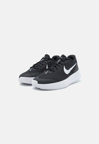 Crne atletske tenisice s teksturiranim pletenim gornjim dijelom, bijelim Nike swoosh logotipom i bijelim potplatom za prijanjanje. Imaju vezice i podstavljen ovratnik.