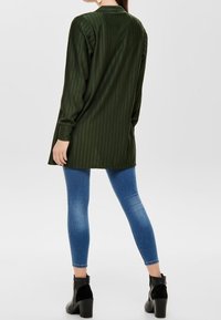 Dunkelgrünes, geripptes Shirt mit langen Ärmeln und geradem Schnitt, kombiniert mit blauen Skinny Jeans und schwarzen Knöchelstiefeln.