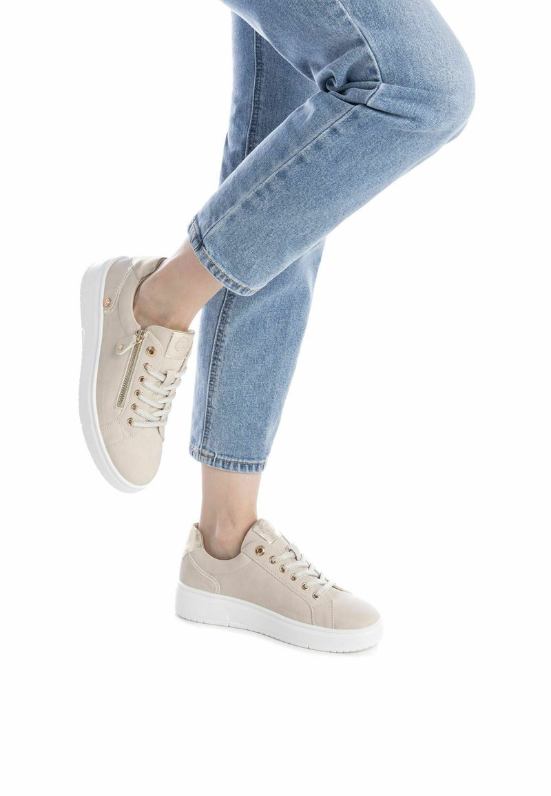 Zapatillas beige de ante con acabado texturizado, que presentan suelas de goma blancas, ojales dorados y un detalle de cremallera lateral.