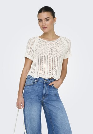 Witte gebreide crop top met korte mouwen, voorzien van een patroon van kleine gaten en een gegolfde onderrand, gecombineerd met hoge taille blauwe wijde jeans.
