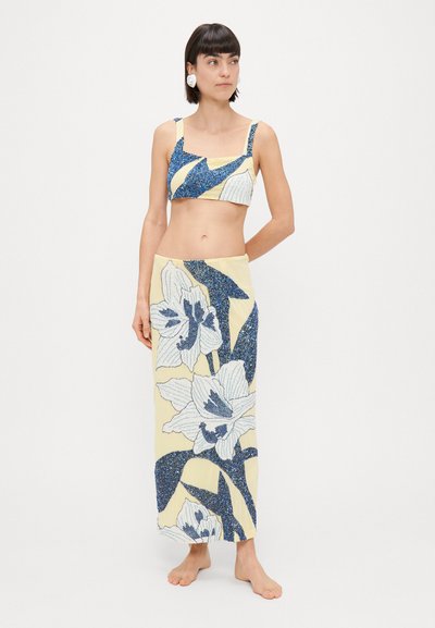 Conjunto de dos piezas que incluye un top corto azul con adornos y una larga falda amarilla con grandes patrones florales blancos. Textura suave, diseño ajustado.
