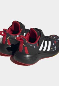 Scarpe sportive con tomaia in tessuto nero e un motivo colorato, dettagli rossi e tre strisce bianche sui lati. Suola in gomma per una buona aderenza.