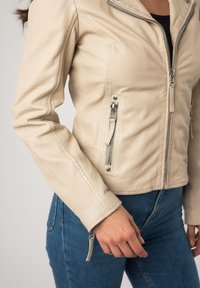 Lichtbeige leren jack met een getailleerd ontwerp, zilveren hardware, ritszakken en een gestructureerde afwerking. Heeft een licht asymmetrische kraag.