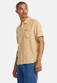 Short-sleeve button-up shirt in light yellow with a geometric pattern. Features a chest pocket and a subtle brand tag. Made of soft fabric.