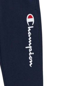 Pantaloni della tuta blu navy realizzati in tessuto morbido, con logo "Champion" ricamato in bianco e accento rosso/bianco in un distintivo circolare.