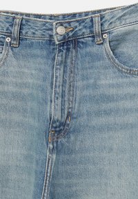 Svijetloplave traperice viskog struka, s pet džepova i bakrenim šavovima. Uključuju metalnu dugmad i mali logo na pojasu.