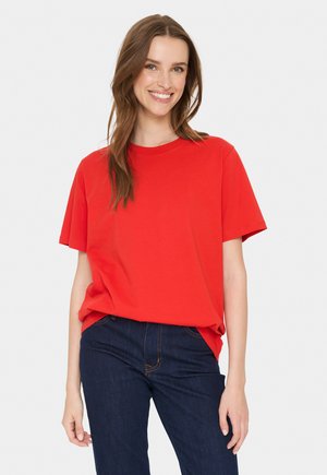 Red cotton t-shirt with short sleeves, a round neck, relaxed fit, textured fabric, worn with dark blue jeans featuring contrast stitching.