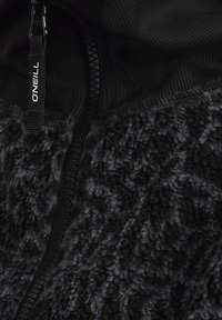 Zwarte textuur fleece stof met een rits en een trekband met het label "O'NEILL" op een zwart kledingstuk.